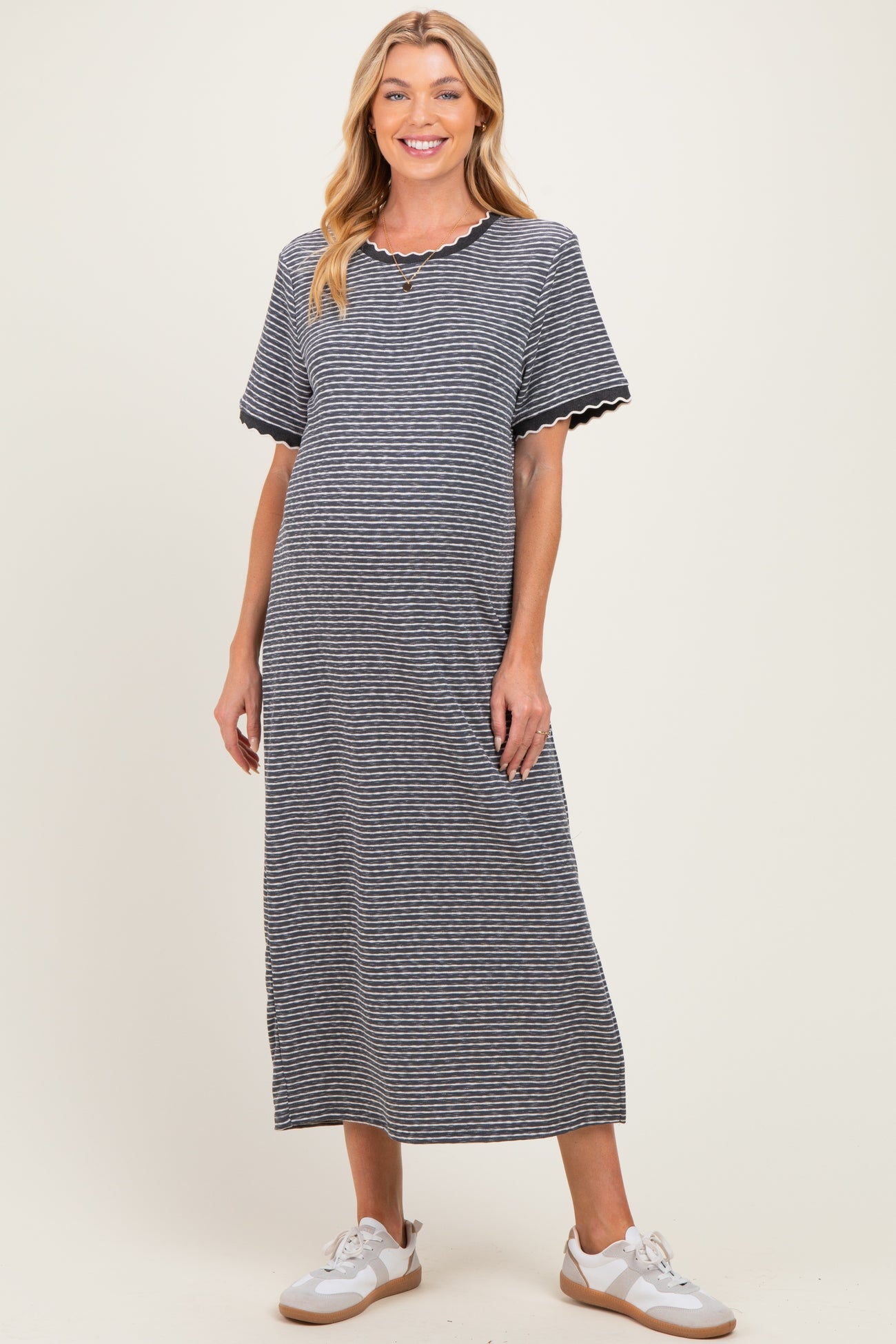 woman wearing a striped maternity maxi dress with short sleeves and a scalloped neckline, displaying her baby bump