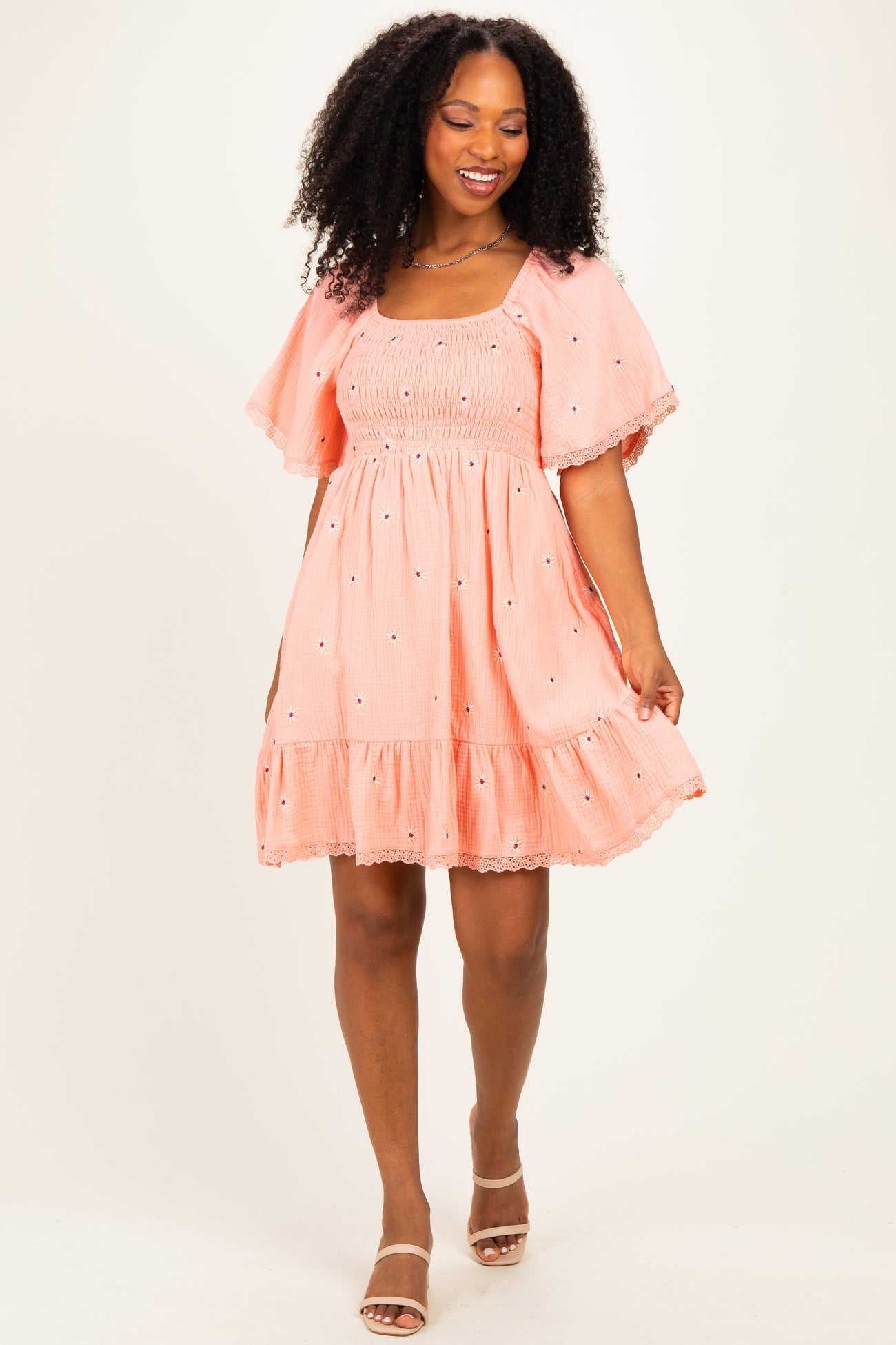 woman wearing a coral puff sleeve mini dress with embroidered flowers and a ruffled hem