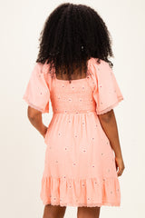 woman wearing a light pink embroidered short dress with smocked bodice and ruffled hem, seen from the back
