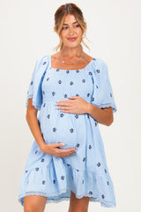 woman wearing a light blue maternity dress with floral embroidery and puff sleeves, holding her baby bump