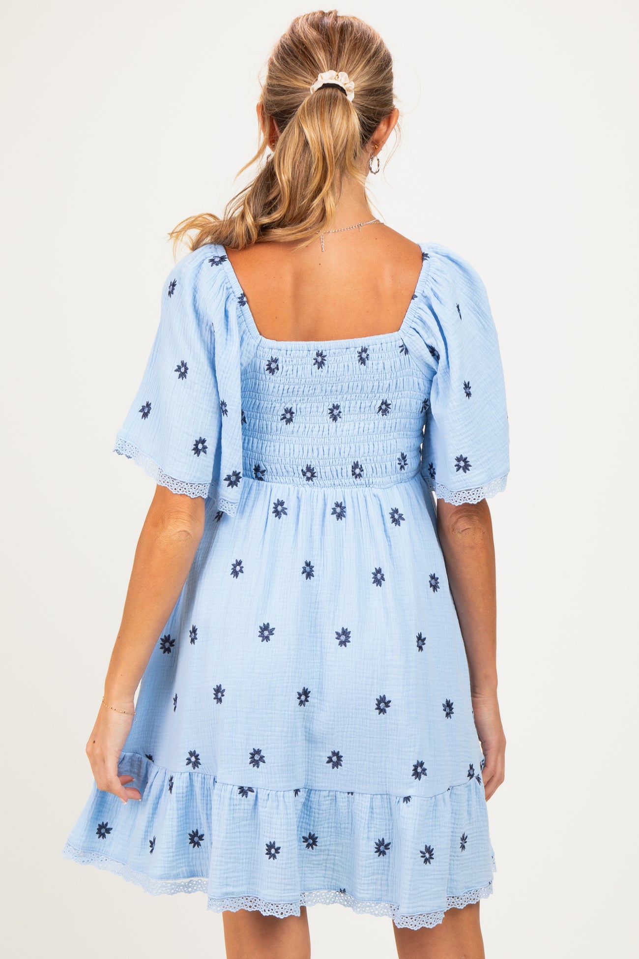 woman wearing a light blue maternity dress with puff sleeves and floral embroidery, showing back view