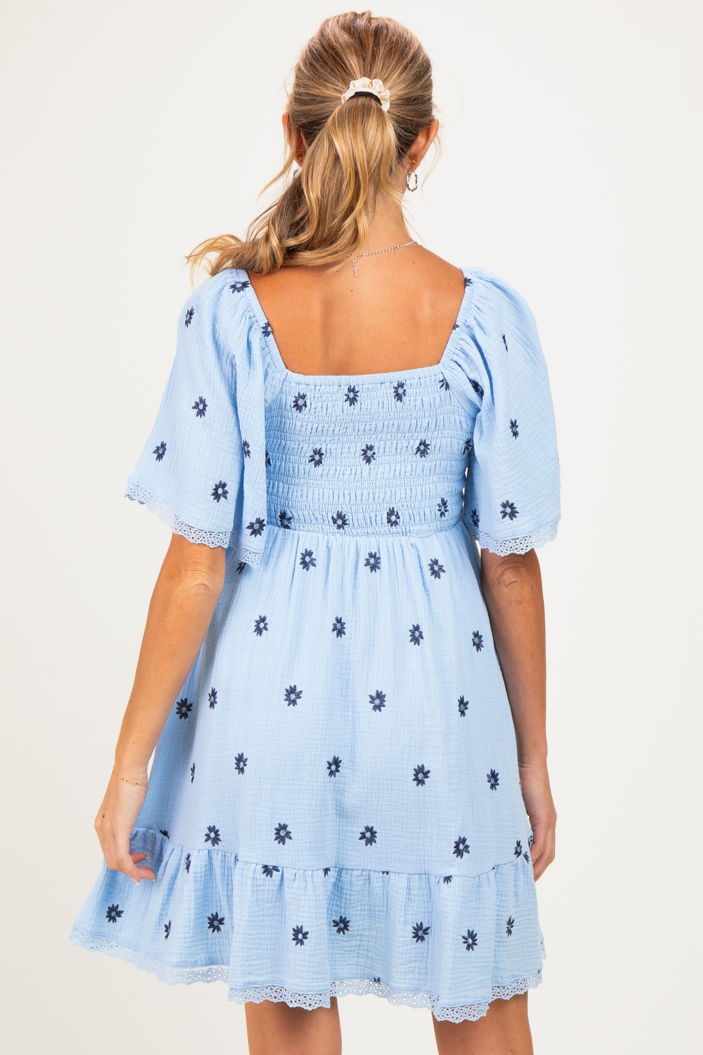 woman wearing a light blue maternity dress with puff sleeves and floral embroidery, showing back view