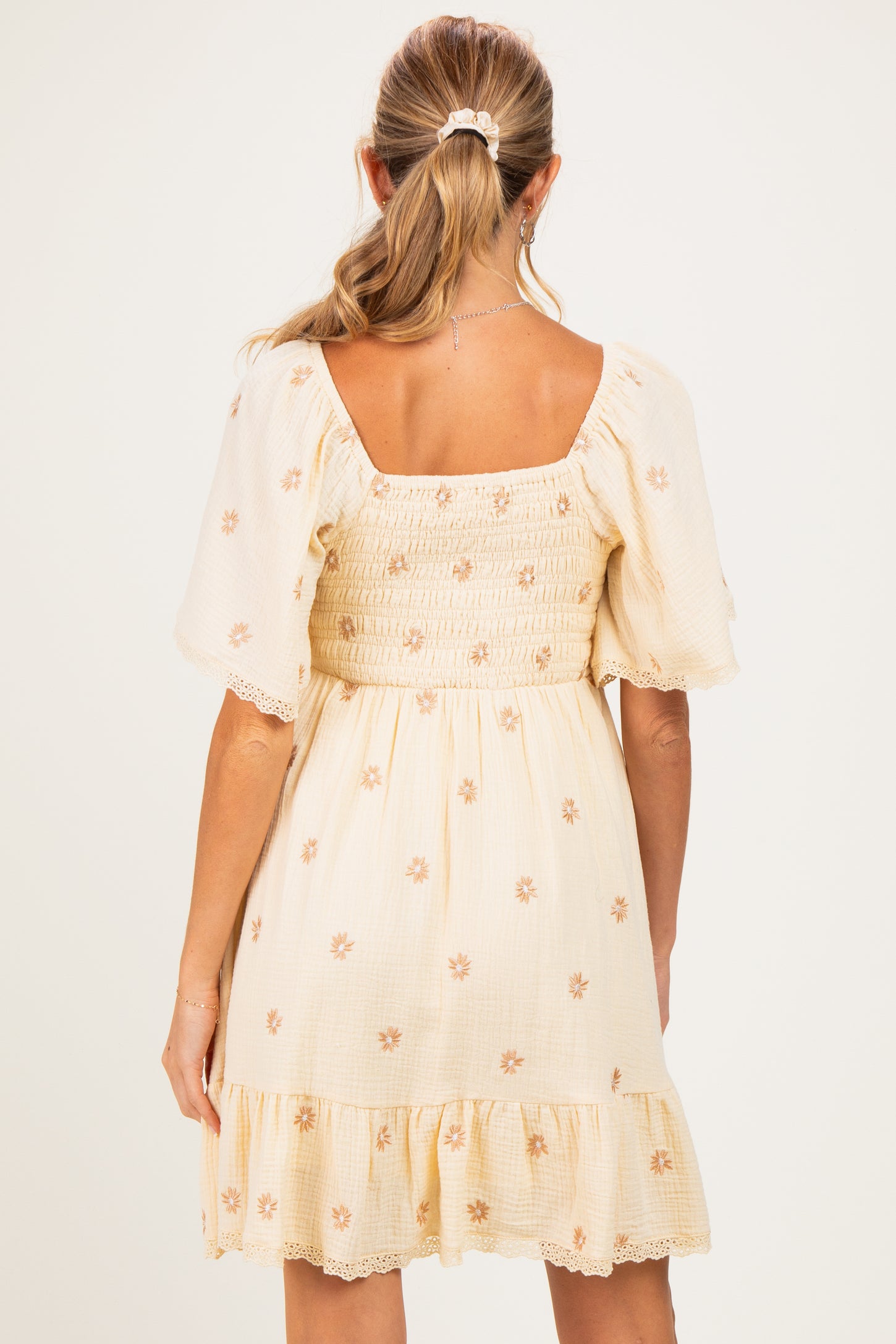 woman wearing a light yellow maternity dress with short puff sleeves and floral embroidery, showing a smocked back design