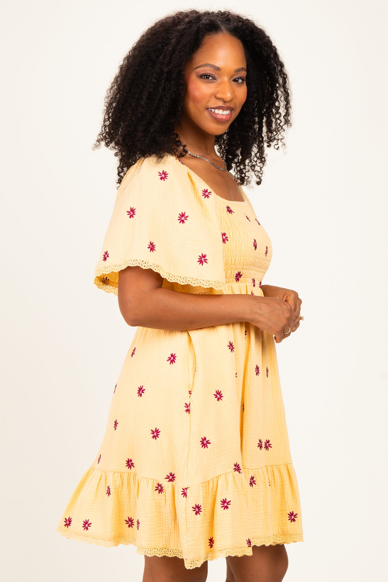 woman wearing a yellow short sleeve dress with floral embroidery and a ruffled hem