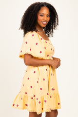woman wearing a yellow short sleeve dress with floral embroidery and a ruffled hem