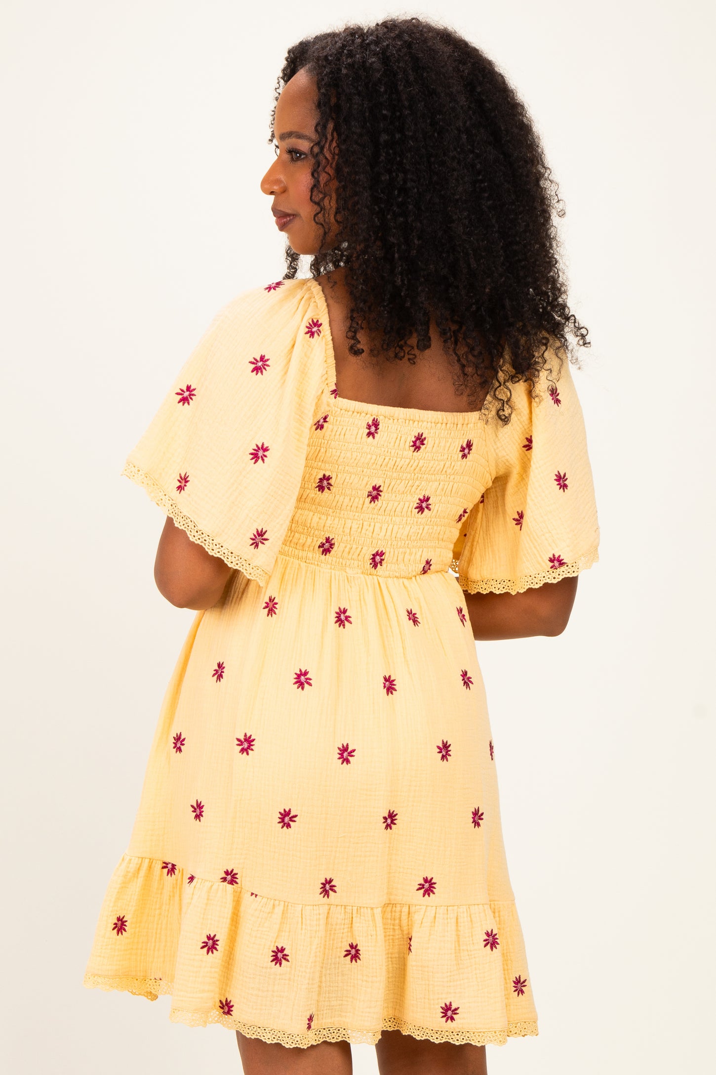 woman wearing a yellow floral embroidered short dress with puff sleeves and a ruffled hem