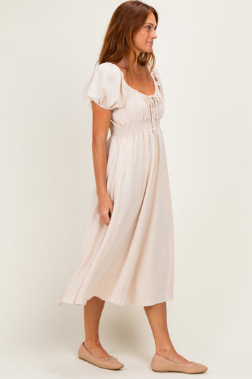 woman wearing a light pink midi dress with puff sleeves and smocked waist, paired with nude ballet flats