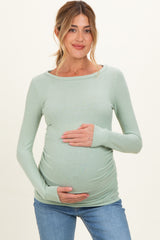woman wearing a light green long sleeve maternity top and holding her baby bump