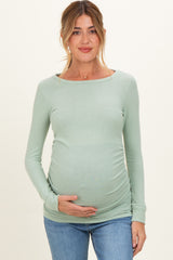 woman wearing a light green long sleeve maternity top and holding her baby bump