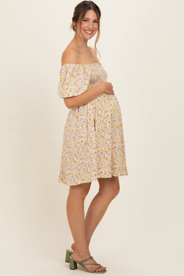 woman wearing a yellow floral off-the-shoulder maternity dress and holding her baby bump