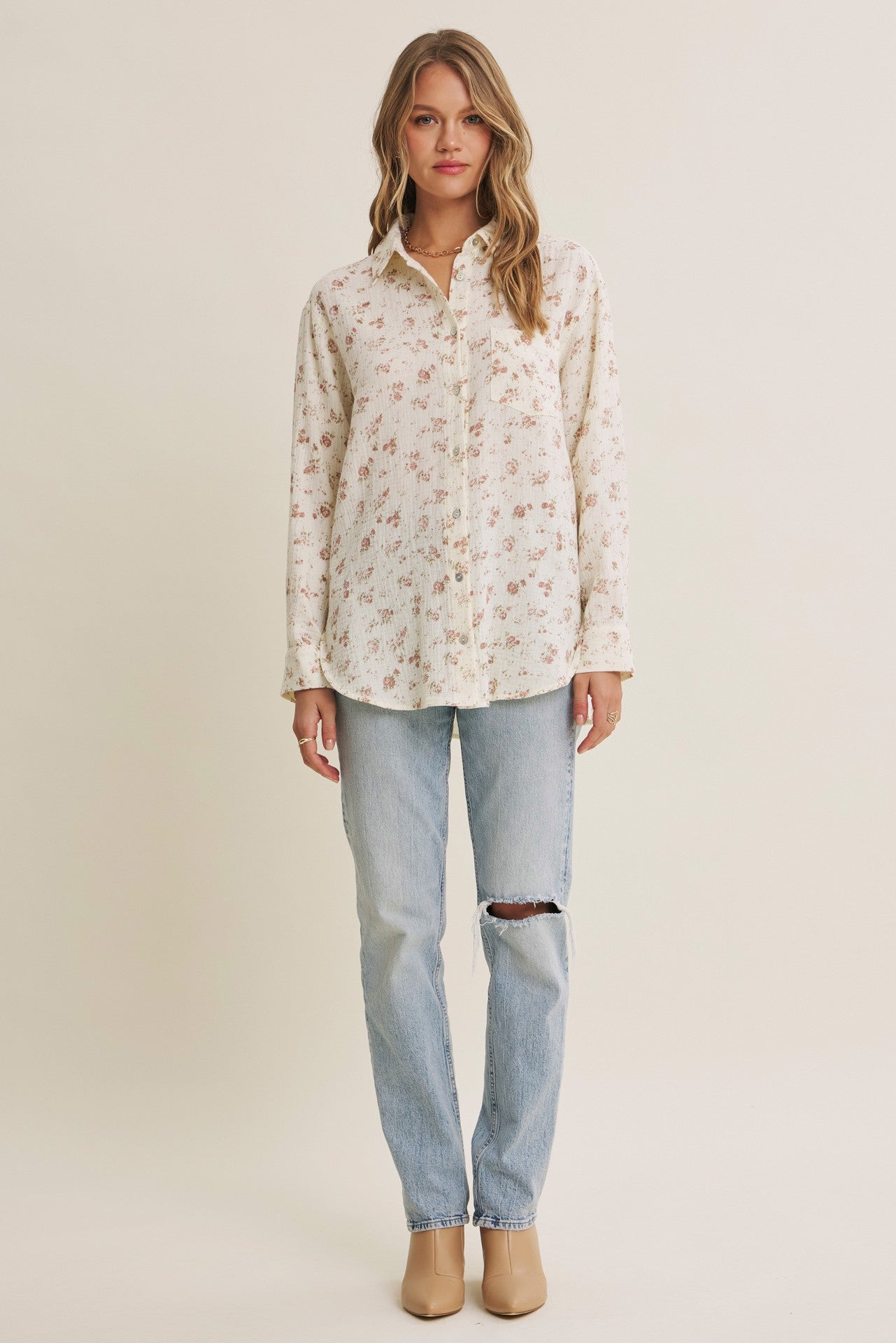 woman wearing a cream button-up shirt with floral print and light wash ripped jeans
