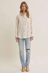 woman wearing a cream button-up shirt with floral print and light wash ripped jeans