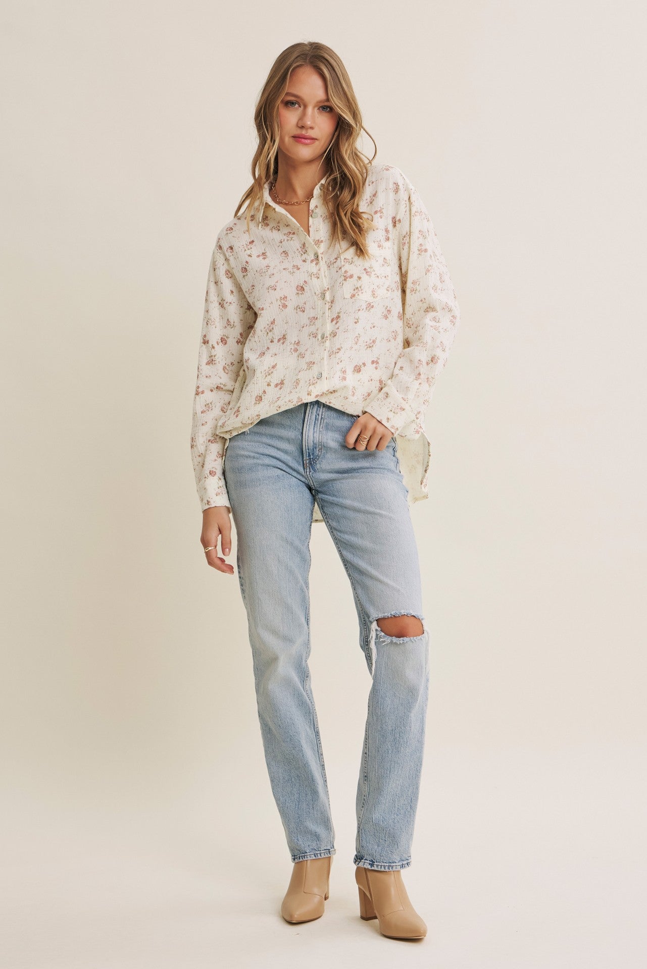 woman wearing a floral print button-up shirt with rolled sleeves and light blue ripped jeans, standing in a casual pose