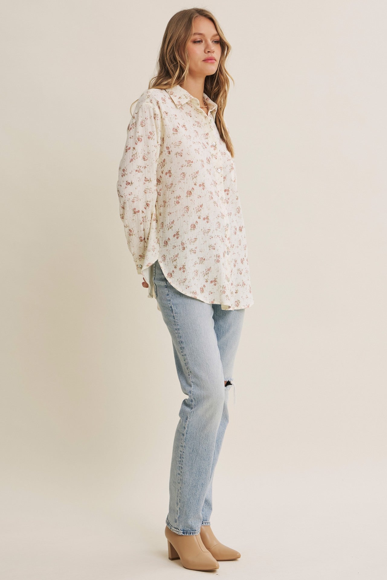 woman wearing a cream floral button-up shirt and light blue distressed jeans with beige heels