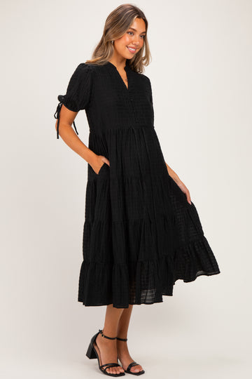 woman wearing a black tiered maternity dress with short sleeves and pockets, styled with sandals and a relaxed fit