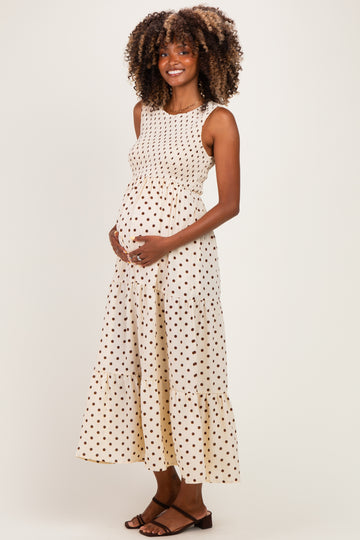 woman wearing a cream maternity dress with brown polka dots and a tiered skirt, gently cradling her baby bump