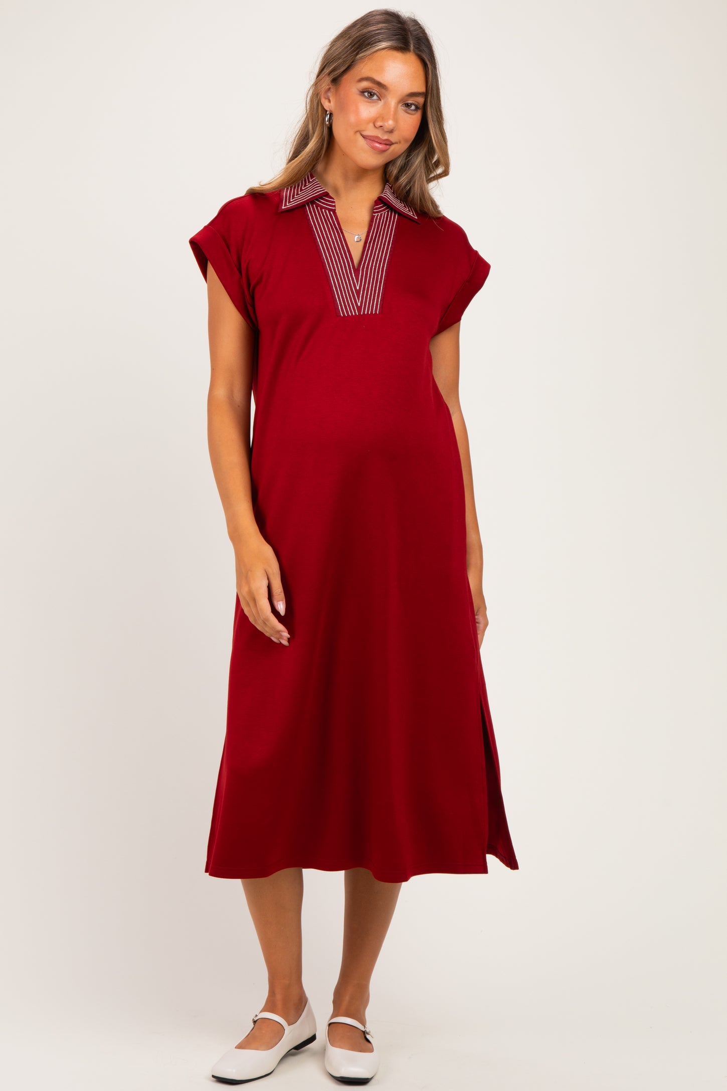 woman wearing a red maternity dress with a striped collar and side slits, showing her baby bump