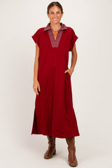 woman wearing a burgundy midi dress with a striped collar and side pockets, standing and smiling