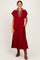 woman wearing a burgundy midi dress with a striped collar and side pockets, standing and smiling