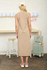 woman wearing a beige sleeveless maxi dress, shown from the back, with a neutral background and pastel accents