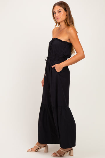 woman wearing a black strapless maxi dress with a tiered skirt and pockets, styled with nude heeled sandals