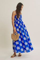 woman wearing a blue maxi dress with white floral print and holding a small woven bag