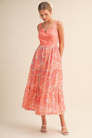 woman wearing a coral sleeveless maxi dress with floral print and tiered skirt