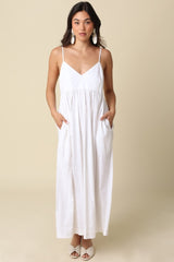 woman wearing a white maxi dress with spaghetti straps and pockets, styled with statement earrings