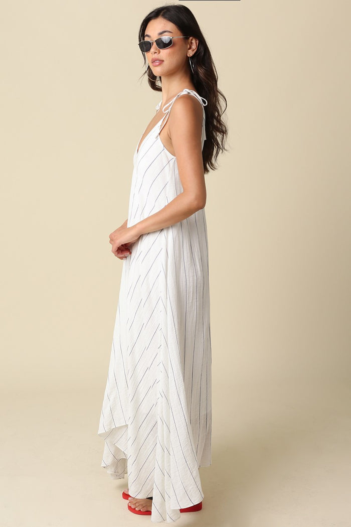 woman wearing a white maxi dress with thin straps and vertical stripes, styled with sunglasses and red heels