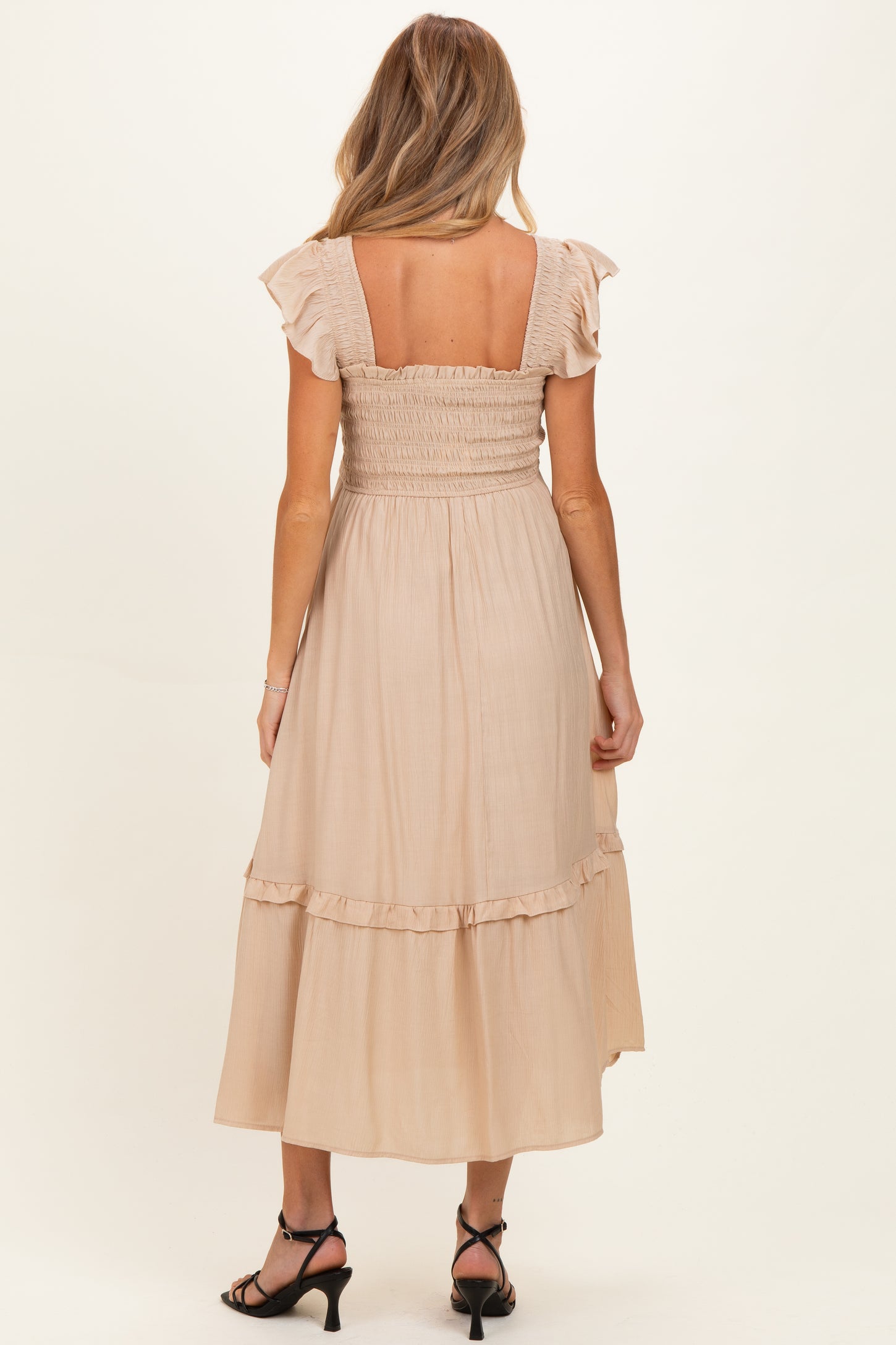 woman wearing a beige maternity dress with ruffle sleeves and a smocked bodice, showing a flowy mid-calf length