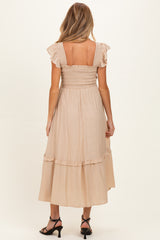 woman wearing a beige maternity dress with ruffle sleeves and a smocked bodice, showing a flowy mid-calf length