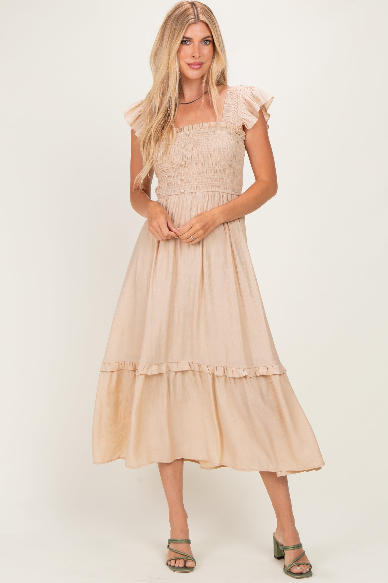 woman wearing a beige smocked maxi dress with ruffled sleeves and tiered hem, standing in a relaxed pose