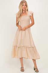 woman wearing a beige smocked maxi dress with ruffled sleeves and tiered hem, standing in a relaxed pose