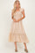 woman wearing a beige smocked maxi dress with ruffled sleeves and tiered hem, standing in a relaxed pose