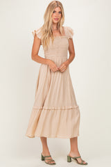 woman wearing a beige smocked midi dress with ruffle sleeves and a tiered skirt, standing in a flowy pose