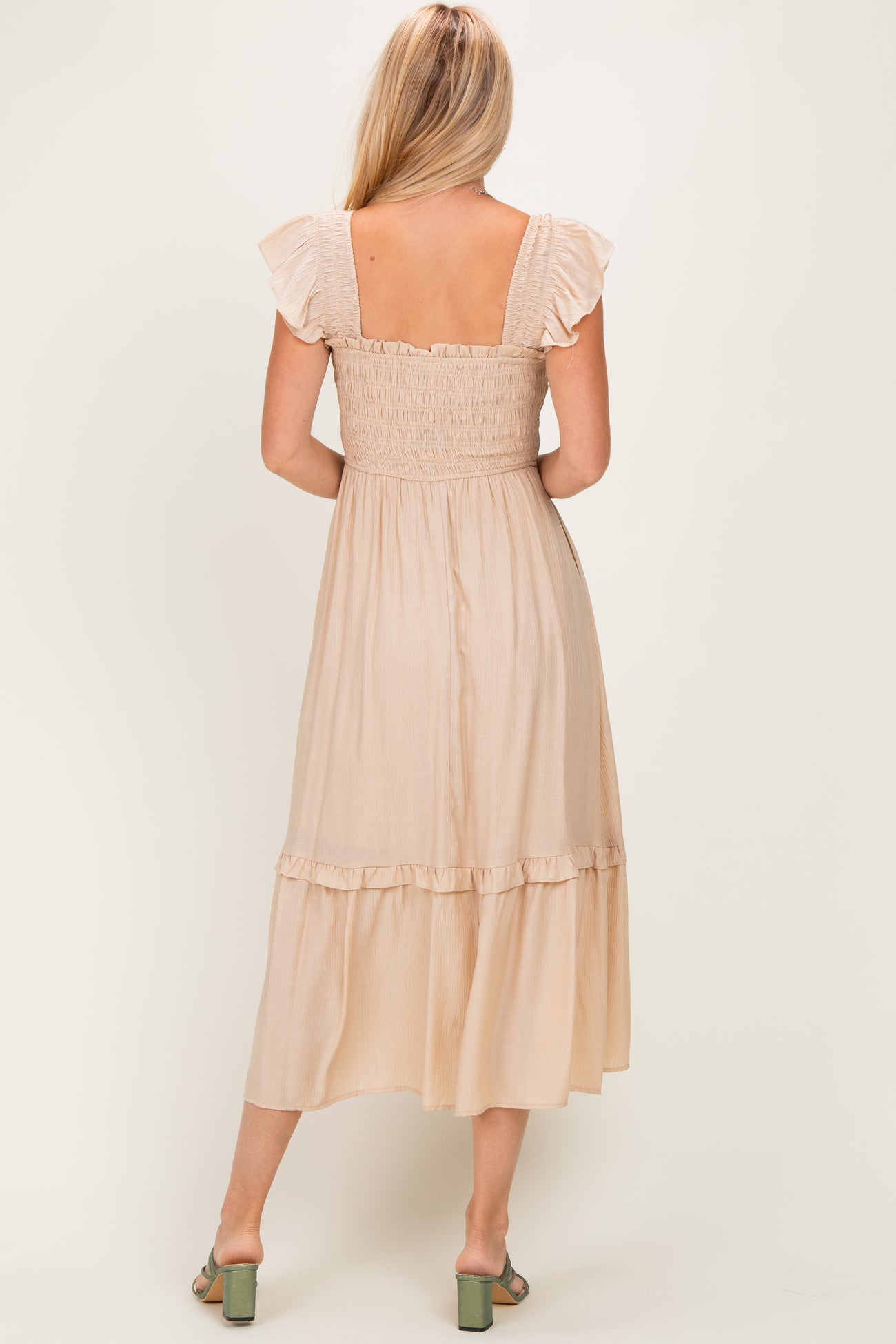 woman wearing a beige midi dress with ruffled sleeves and a smocked back, showing the tiered skirt from the back