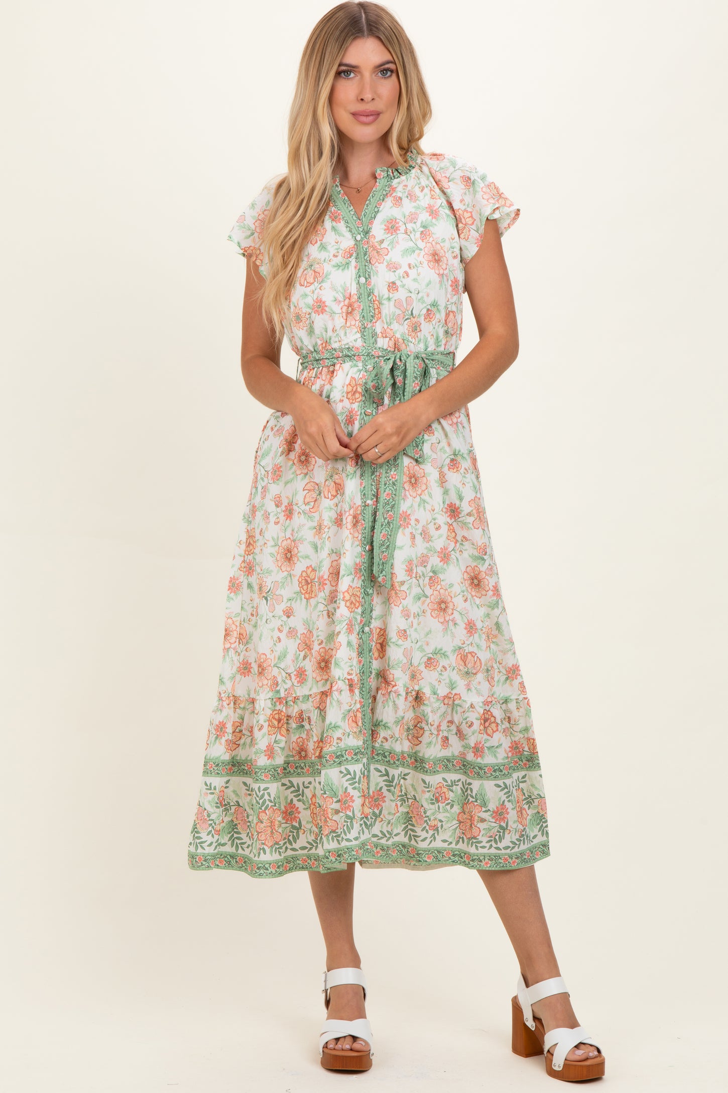 woman wearing a floral midi dress with cap sleeves and a tie waist in shades of orange and green
