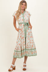 woman wearing a floral print midi dress with short sleeves, a tie waist, and pockets in a light color scheme