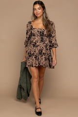 woman wearing a beige floral maternity dress with puff sleeves and a fitted bodice, holding a green cardigan