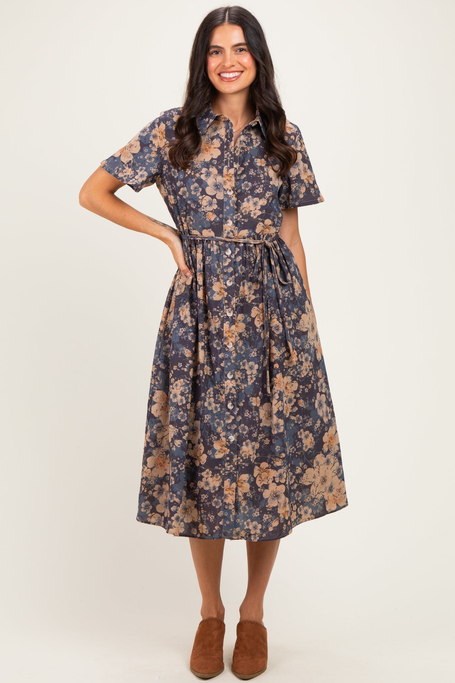 woman wearing a navy floral midi dress with short sleeves and a belt, standing with hands in pockets