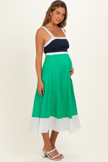 woman wearing a navy and white maternity top with a green and white midi skirt, holding her baby bump