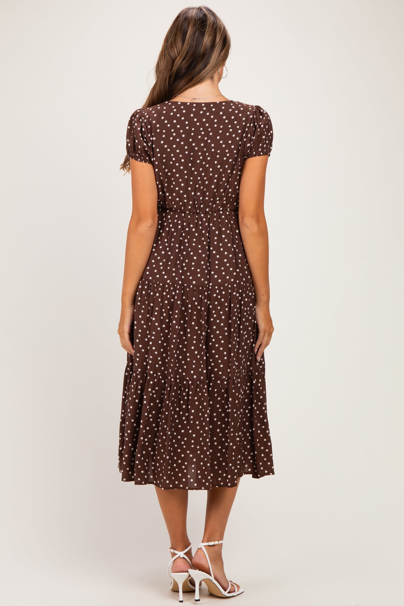 woman wearing a brown polka dot maternity dress with short sleeves and a tiered skirt, seen from the back