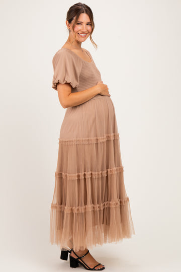 woman wearing a blush pink maternity maxi dress with puff sleeves and tiered tulle detail, holding her baby bump