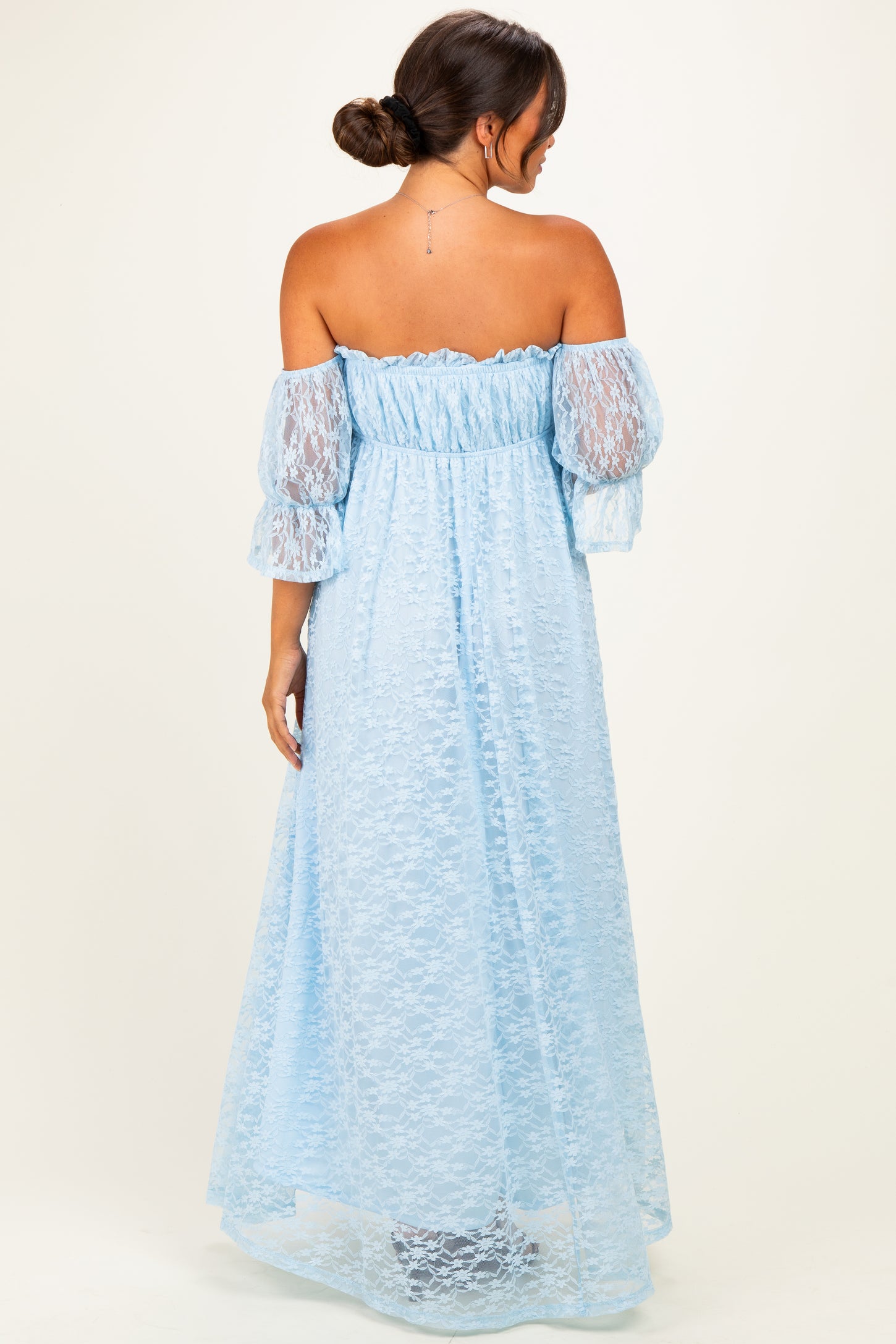 woman wearing a light blue off-the-shoulder maternity gown with sheer lace sleeves and a flowing skirt