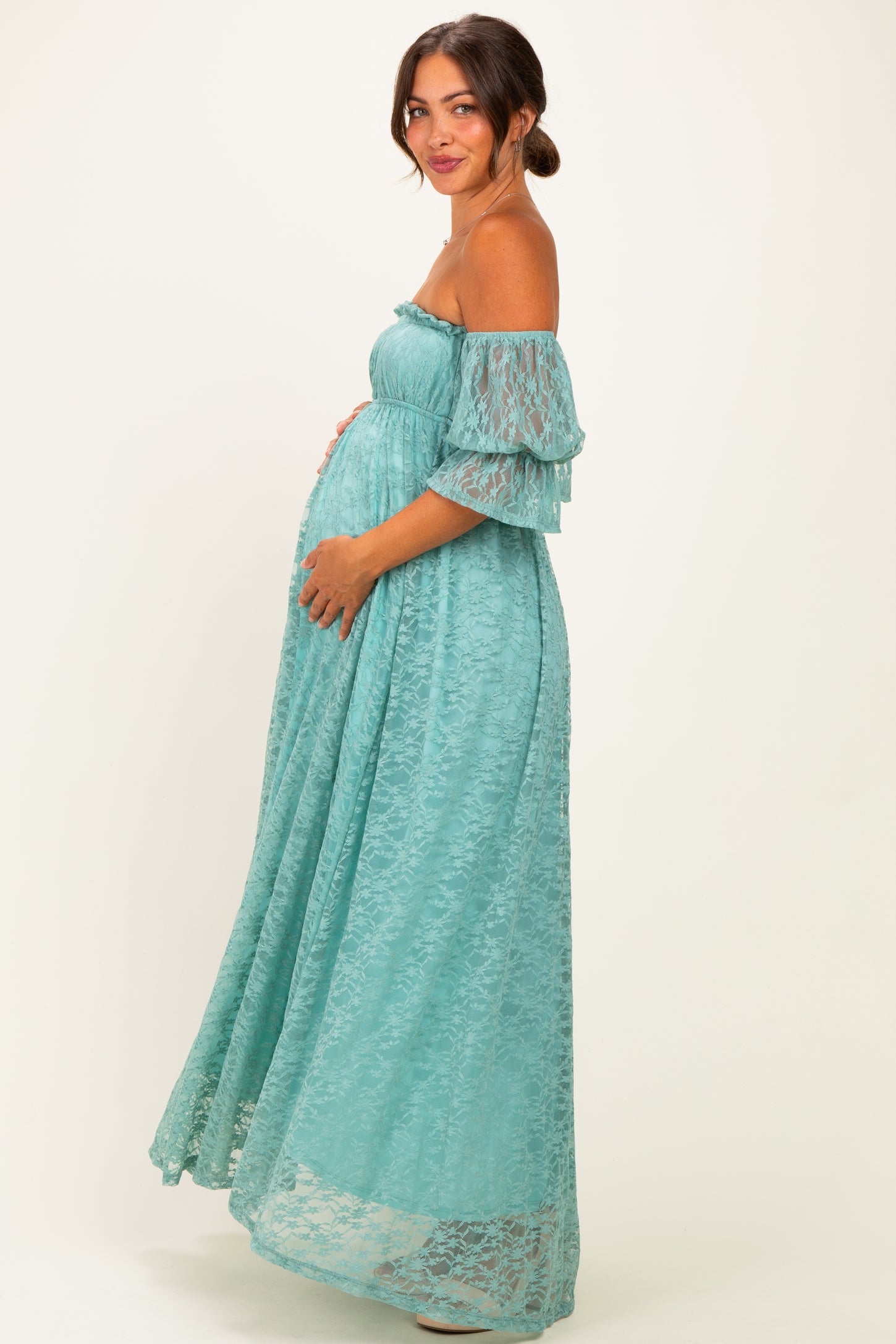 woman wearing a light turquoise lace off-the-shoulder maternity gown and holding her baby bump
