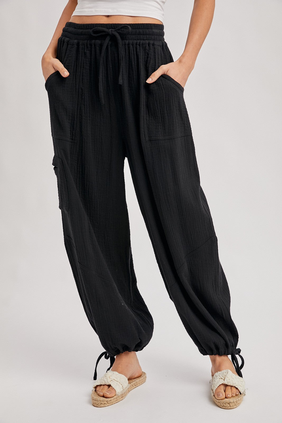 woman wearing black relaxed fit pants with pockets and drawstring hem, paired with white sandals