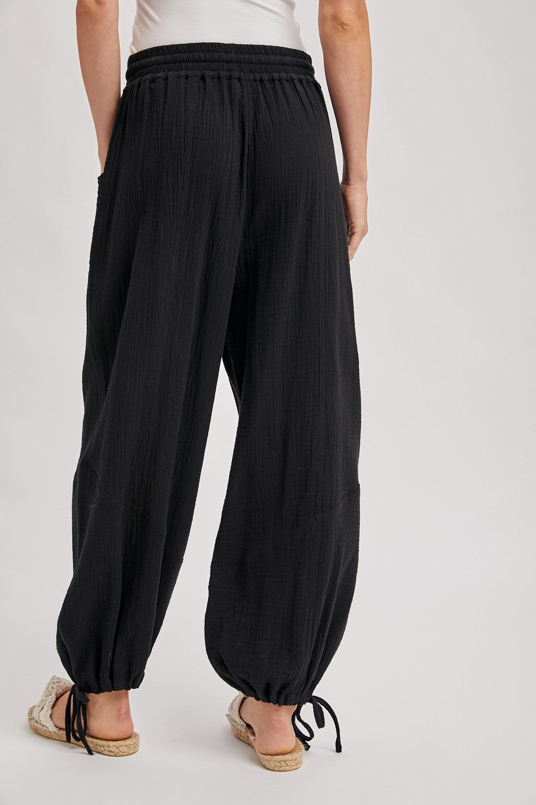 woman wearing black loose-fit jogger pants with an elastic waistband and drawstring cuffs, viewed from the back