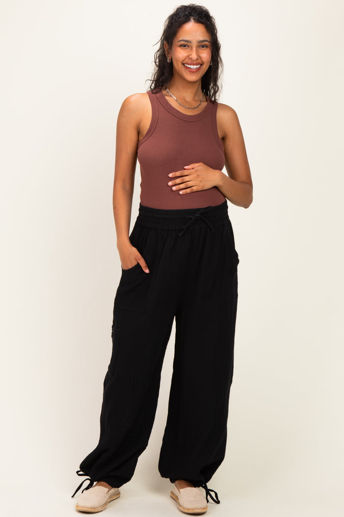 woman wearing a rust ribbed maternity tank top and black loose-fitting maternity pants, holding her baby bump