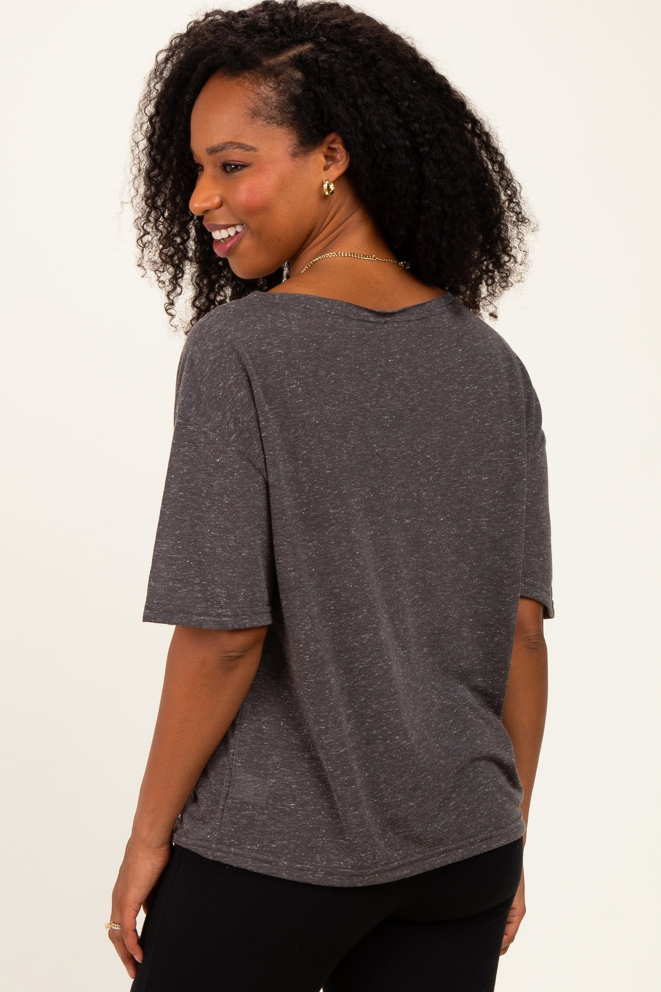 woman wearing a loose-fitting charcoal gray short sleeve t-shirt, smiling and facing sideways