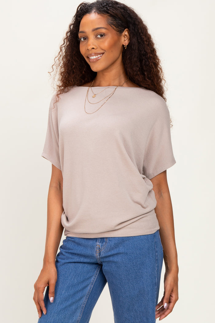 woman wearing a taupe short sleeve top with a relaxed fit paired with blue denim jeans and layered necklaces